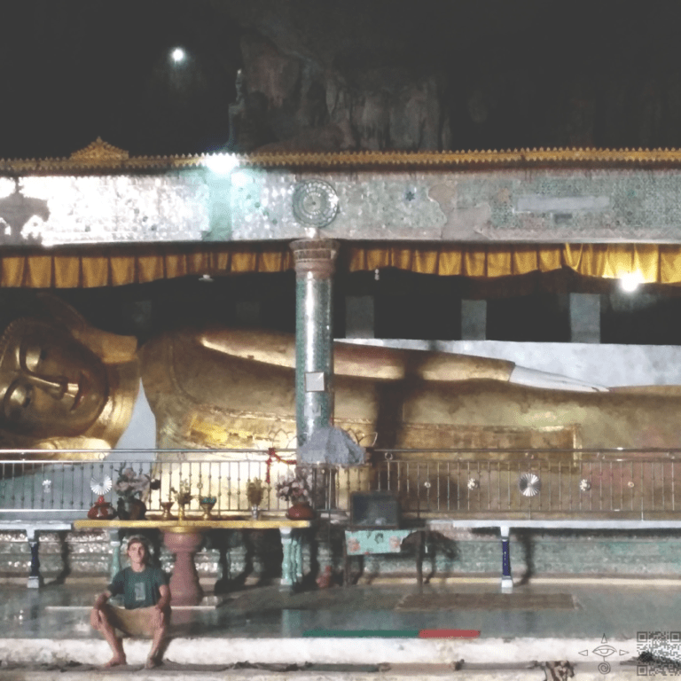 Man sits, cavern, in front of Golden Buddha. Buddha statue cave.
